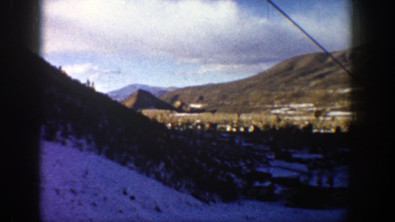 High vantage view over Aspen, Colorado in 1961, with forested snow slopes, valley buildings, and rounded mountains beyond.