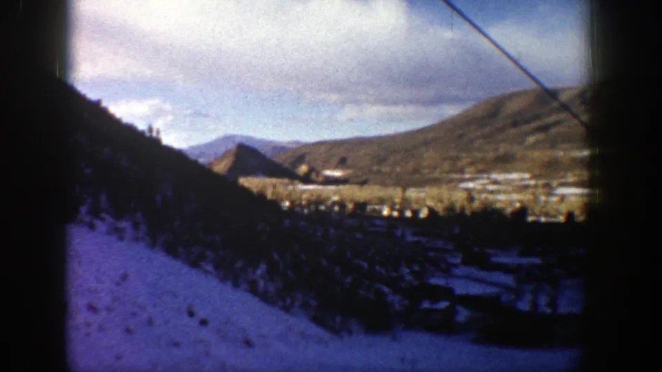 Aspen, Colorado valley view from 1961 home-movie footage, with snow, evergreen trees, distant buildings, and muted winter light.