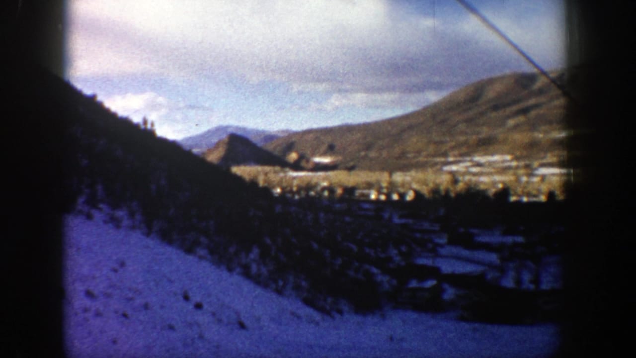 1961 8mm view of a snow-covered Aspen-area mountain valley with hills, trees and resort grounds framed by dark film edges.