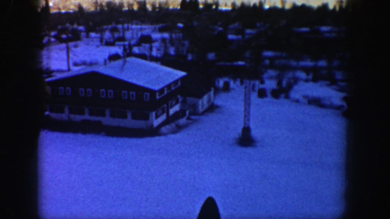 Snow-covered lodge building and ski-lift tower seen from above.