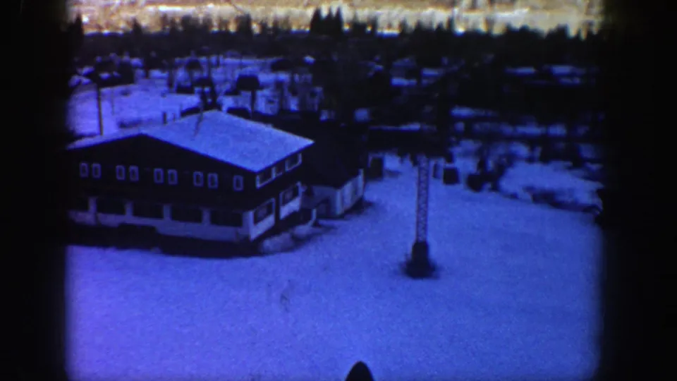 Blue-tinted 8mm frame showing an Aspen-area lodge-style building, ski-lift tower and surrounding snow-covered resort grounds.