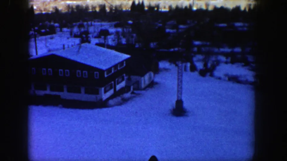 1961 Aspen-area 8mm view of a lodge, ski-lift tower, broad snowfield and dark background trees with heavy vignette edges.
