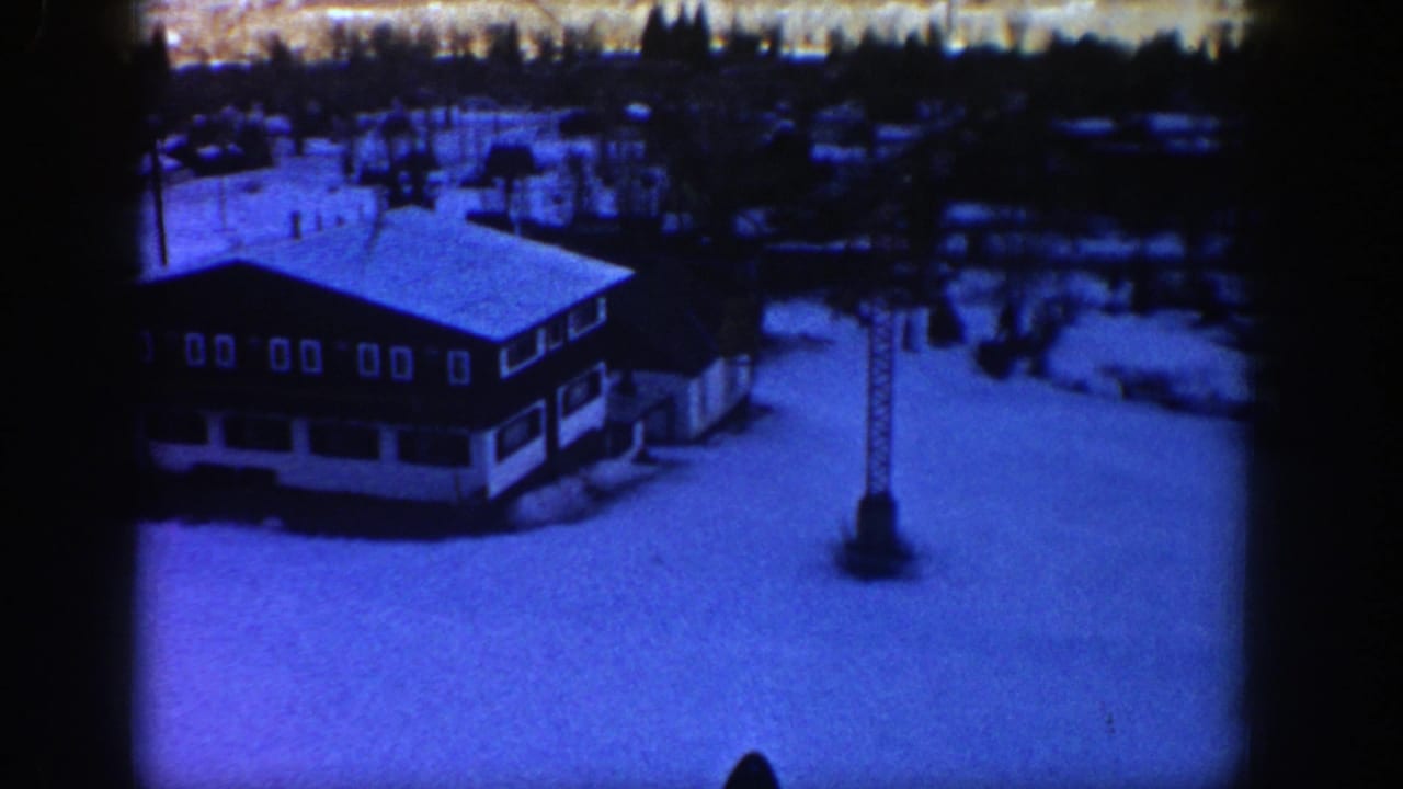 Snow-covered lodge and ski lift tower beside a broad ski slope.