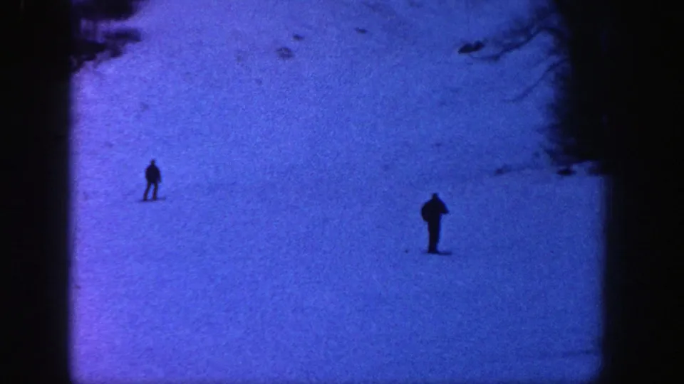 1961 Aspen frame with two distant skiers standing or moving across a wide snow-covered ski hill.