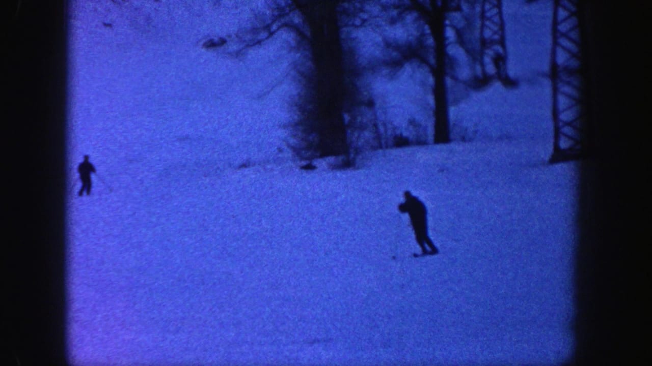 Skiers in dark clothing cross a blue-tinted snowy Aspen hillside, with trees and a lift tower visible in the background.