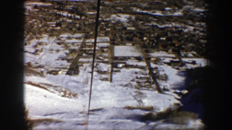 Aerial view over a snow-covered Aspen valley with roads, buildings, and dark film-frame borders.