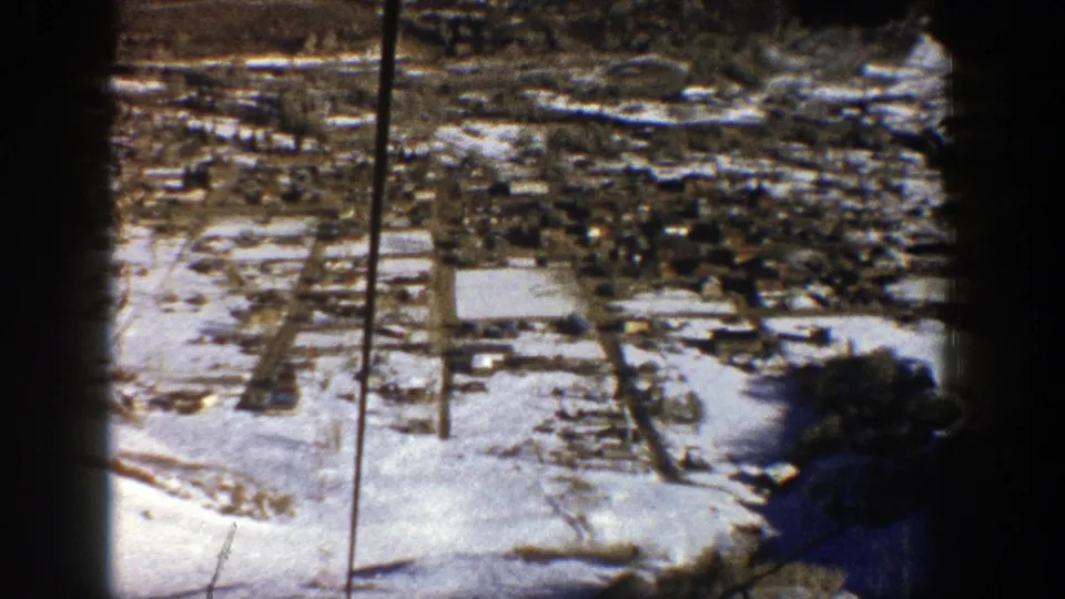 Snow-dusted Aspen valley appears from above in grainy 8mm footage, with roads and buildings visible below.