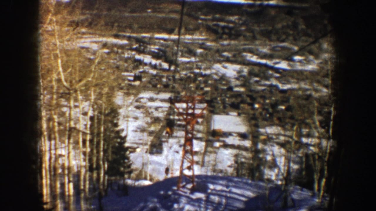 1961 Aspen, Colorado 8mm frame showing a chairlift descending past a red tower on a snowy slope with bare aspen trees.