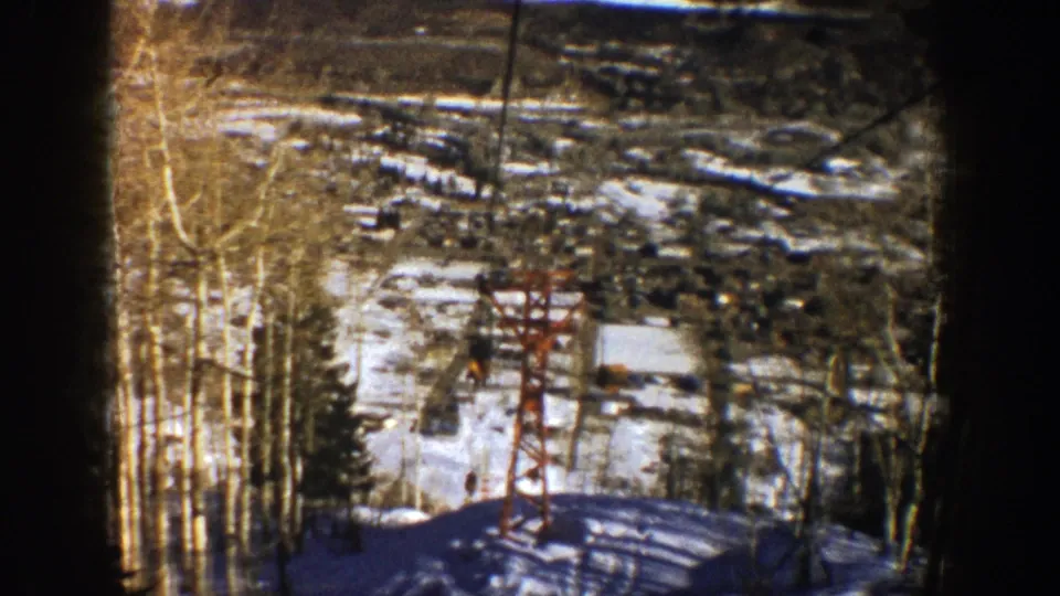1961 Aspen, Colorado 8mm frame showing a chairlift descending past a red tower on a snowy slope with bare aspen trees.