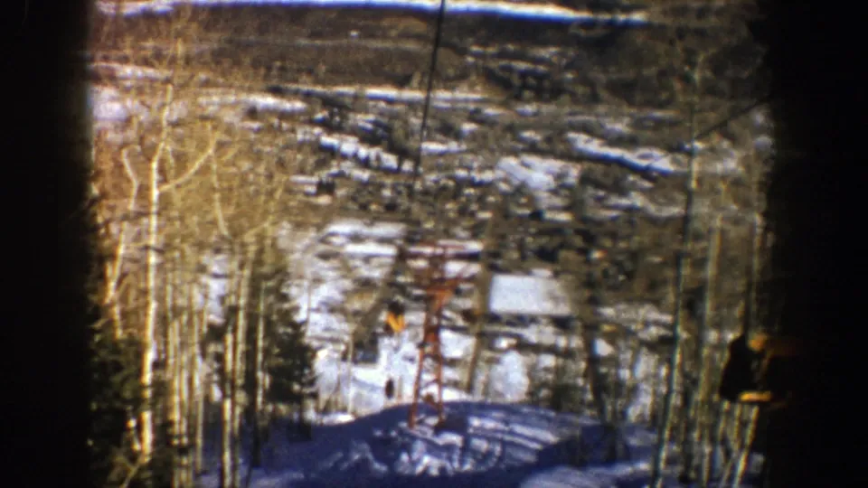1961 Aspen, Colorado 8mm frame showing the red chairlift tower, snowy slope, bare aspen trees, and a distant skier figure.