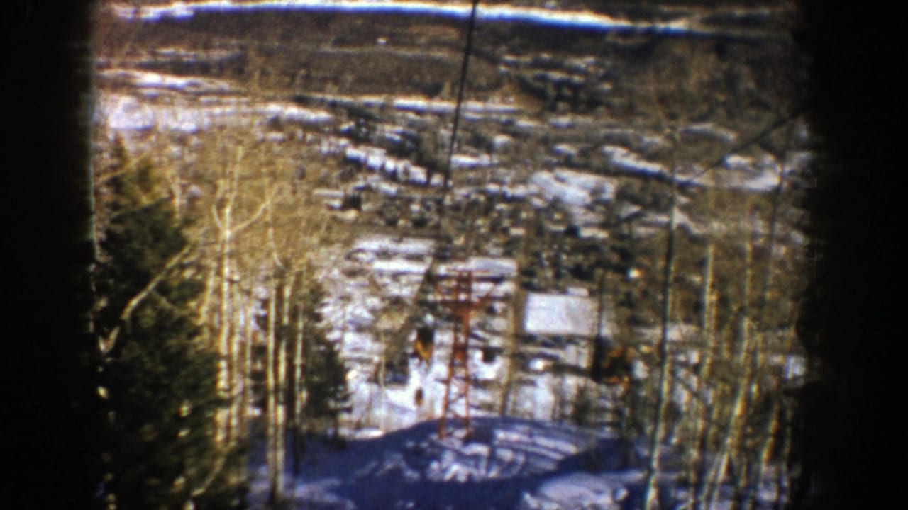 Snowy ski area viewed through trees with a red chairlift tower below.