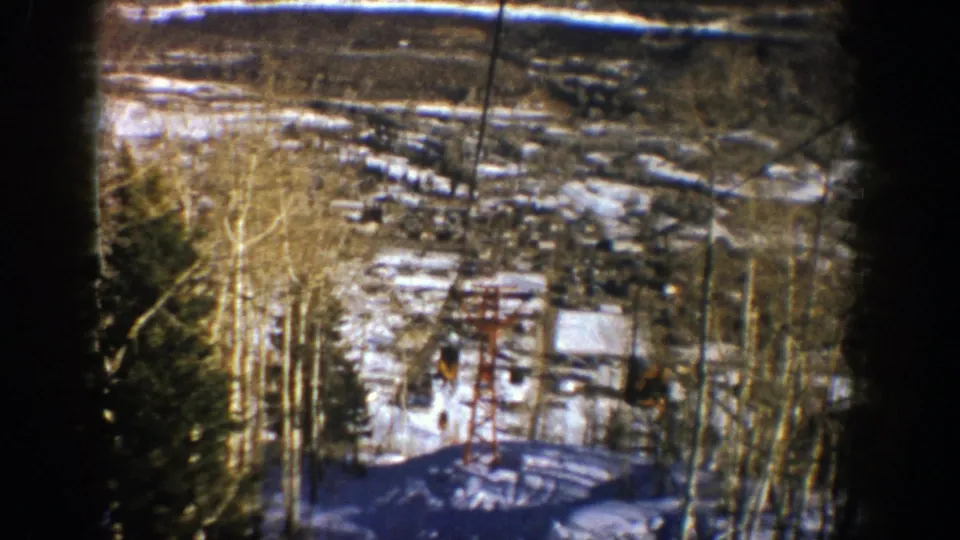 1961 Aspen ski-area view from above, showing snow, bare aspen trees, lift cables, and a red chairlift tower.