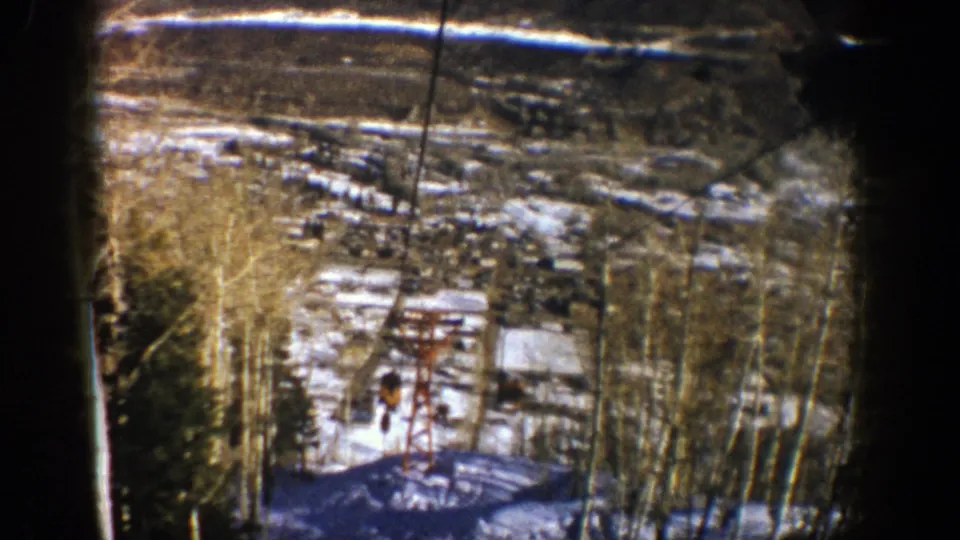 1961 Aspen ski-area panorama with a red lift tower, snow-covered ground, bare trees, and distant resort structures.