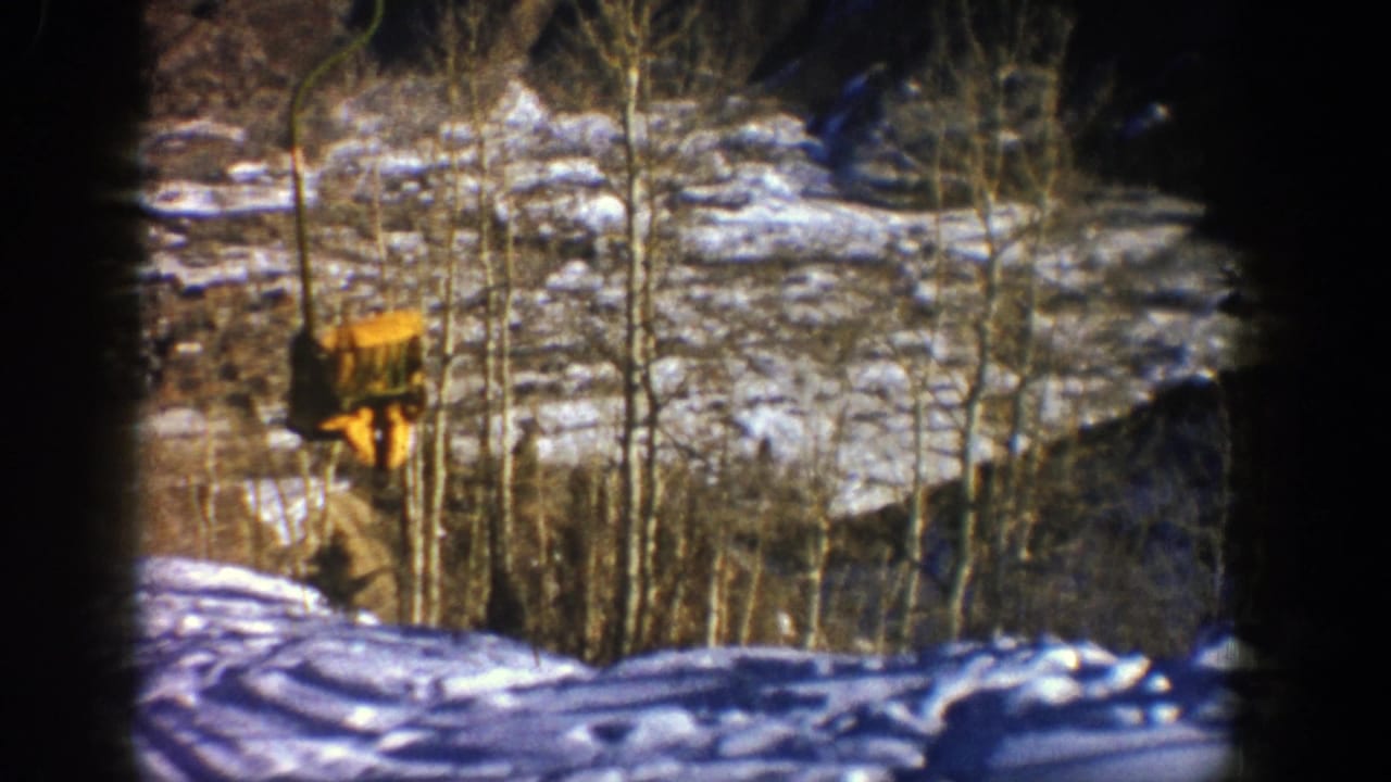Yellow ski-lift chair passing over a snowy slope with bare trees and dark 8mm frame edges.