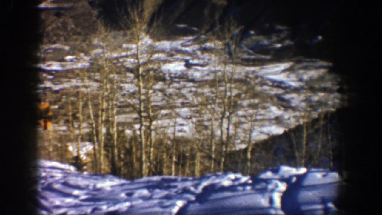 Snowy mountainside with bare trees and a small yellow lift chair partly visible at left.