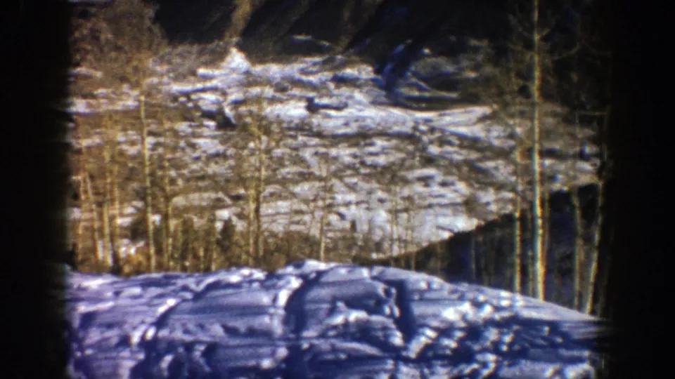 1961 Aspen, Colorado home-movie frame showing snowy terrain, bare aspen trees, and dark projected-film borders.