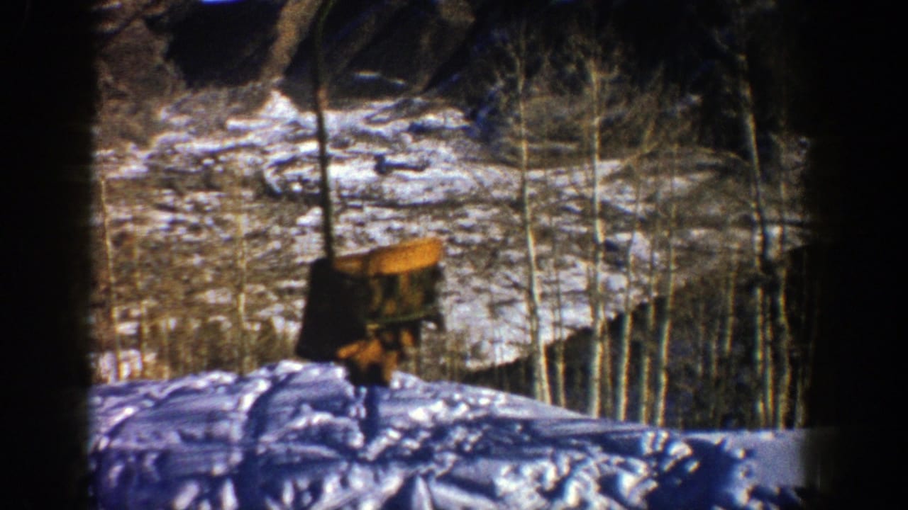 Empty lift chair passing above a snowy slope with bare trees.