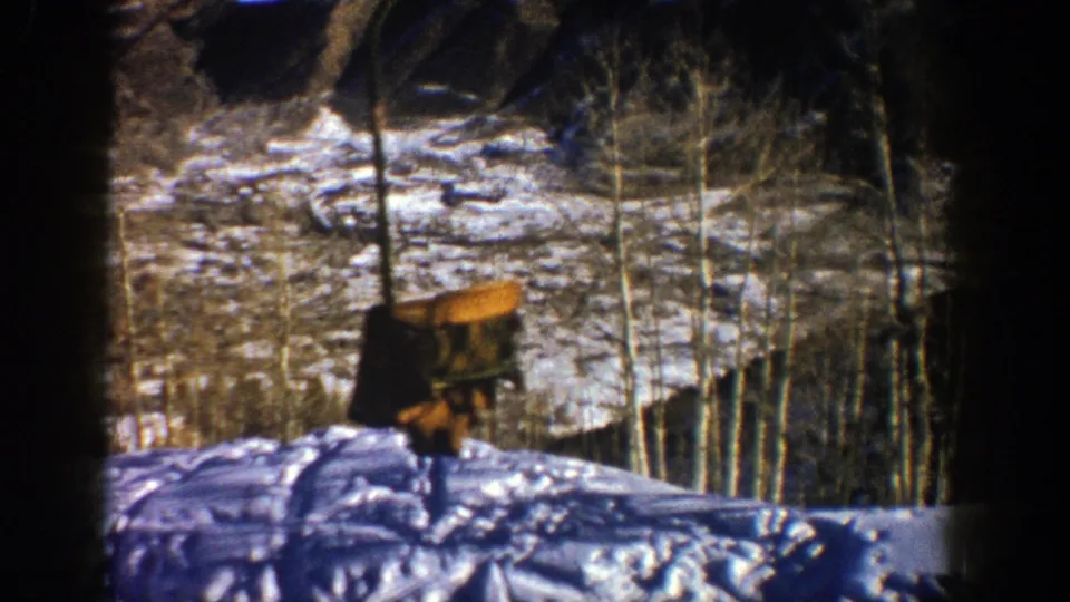 1961 Aspen 8mm frame with an empty chairlift seat crossing a snow-covered slope lined by leafless aspen trees.