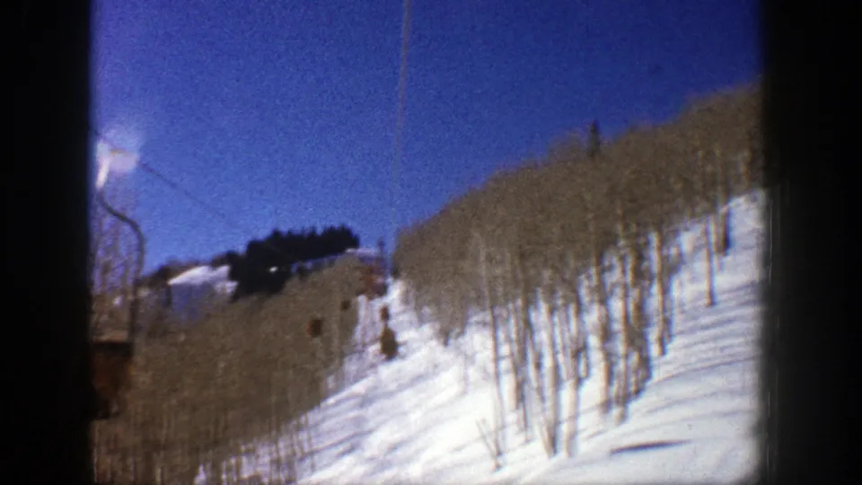Aspen, Colorado 1961 home-movie frame showing blue sky, a snowy ski slope, and leafless aspen trees from a lift perspective.
