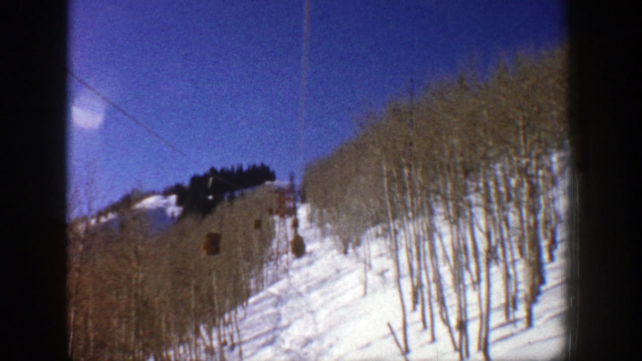 Aspen, Colorado ski-lift view from 1961 with brown cabins on the cable above snow and leafless trees.