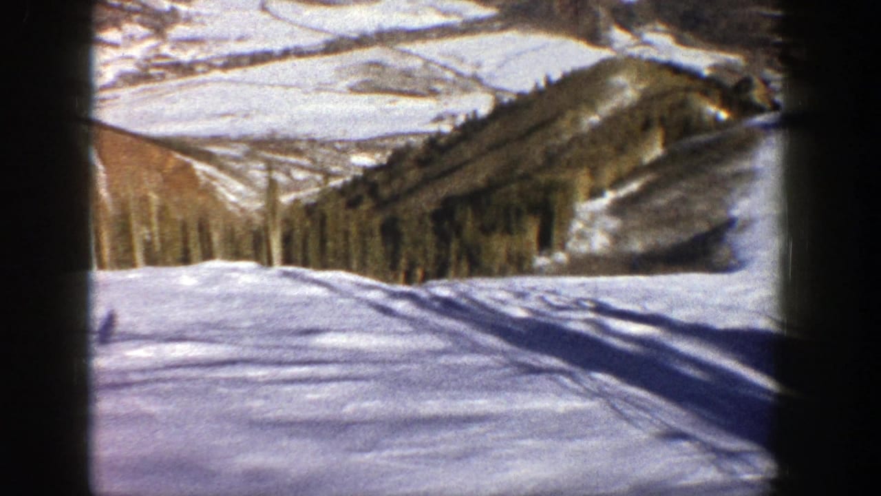 Snowy slope with tree-lined hillsides and distant mountain terrain beyond the run.