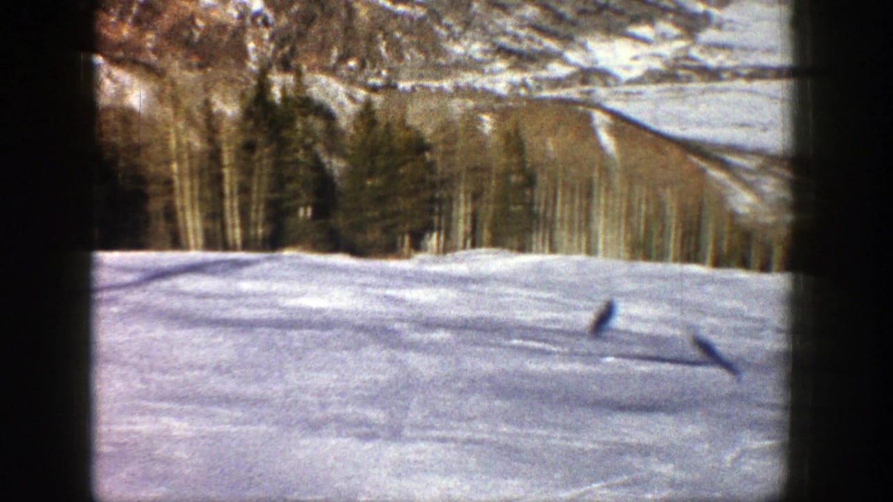 1961 Aspen, Colorado 8mm frame showing a snowy open field, long shadows, forest edge, and snow-dusted mountain slope.
