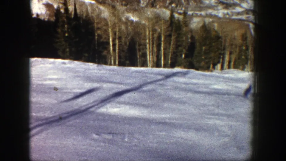 1961 Aspen, Colorado 8mm frame showing rippled snow, crossing shadows, dense trees, and a partially snow-covered mountainside.