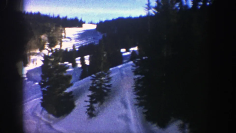 Vintage 8mm Aspen-area frame showing a snowy hillside, open ski-like tracks, and evergreen trees with pronounced home-movie grain.
