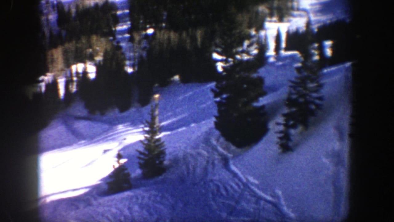 1961 Aspen 8mm frame showing a snowy ski run bordered by evergreens, with tracks and strong winter shadows.