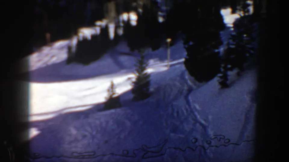 1961 Aspen 8mm frame of a shadowed ski slope with evergreen borders and curving tracks in bright snow.