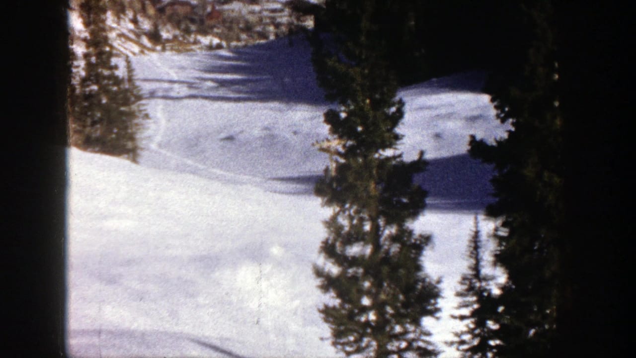1961 Aspen home-movie frame showing a snow-covered mountain slope partly framed by tall evergreen trees.