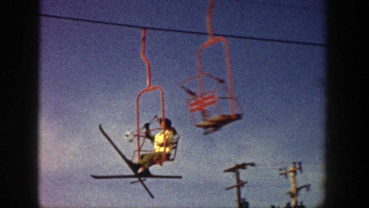 Aspen, Colorado 1961 home-movie frame showing a skier on a red chairlift with skis angled outward against blue sky.