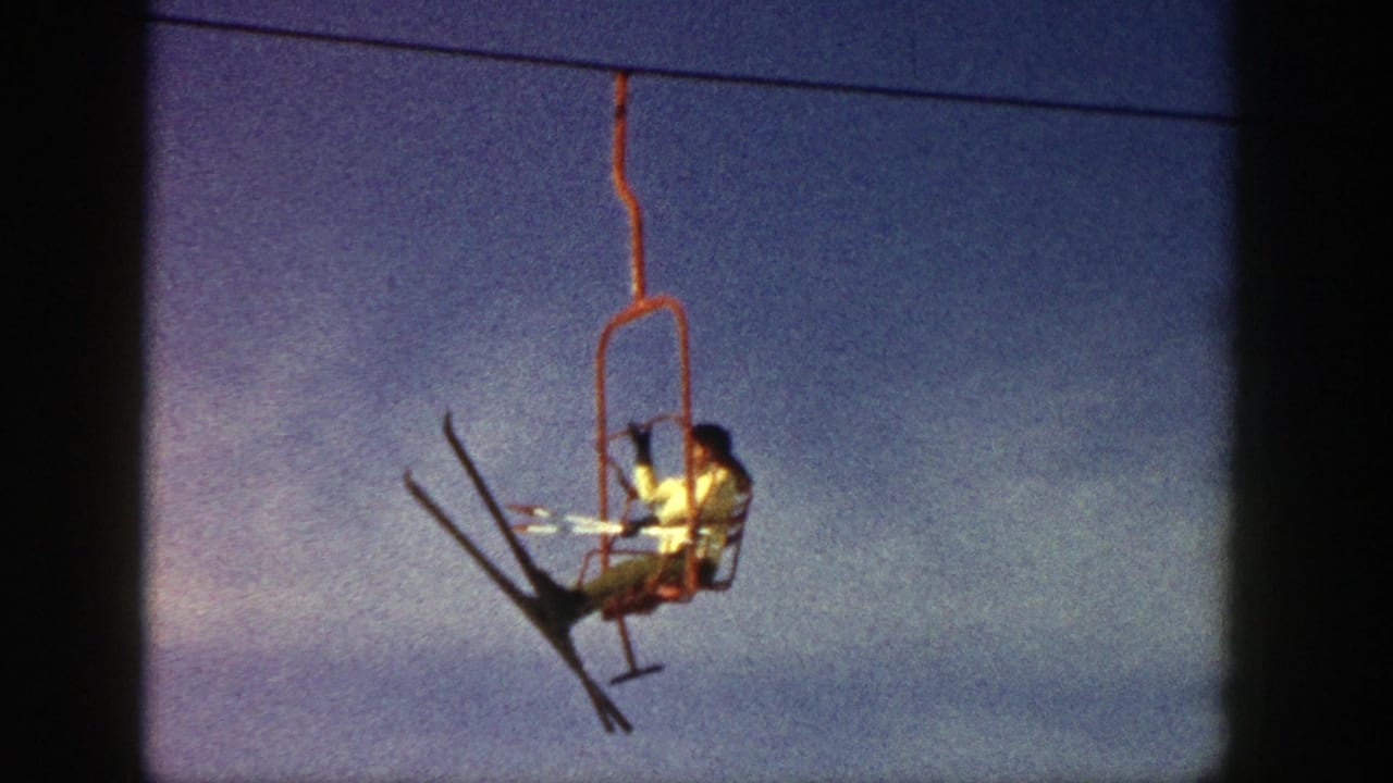Skier on a red chairlift suspended against a blue sky.