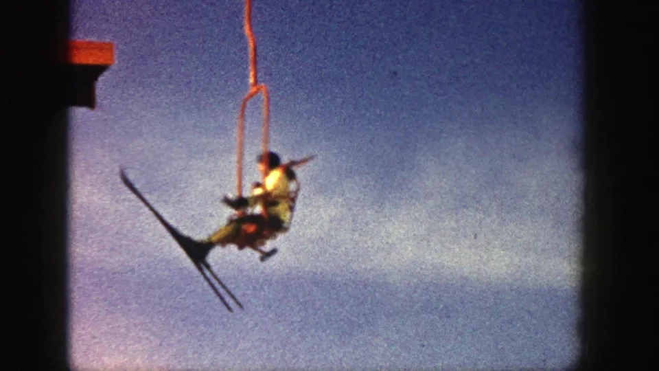 Aspen 1961 8mm frame showing a skier on a red chairlift, with skis and chair hardware visible against the sky.