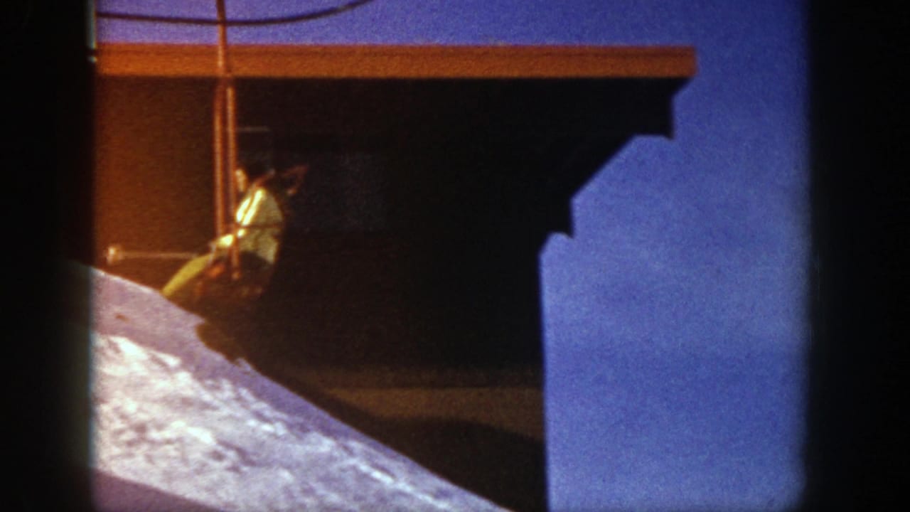 Chairlift rider passing above a bright snowy slope near a dark structure.