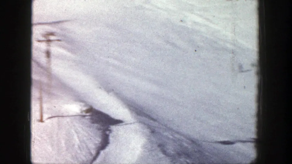 A high-angle 8mm view of the Aspen snow slope shows a pole, tracked powder, and pale winter light.