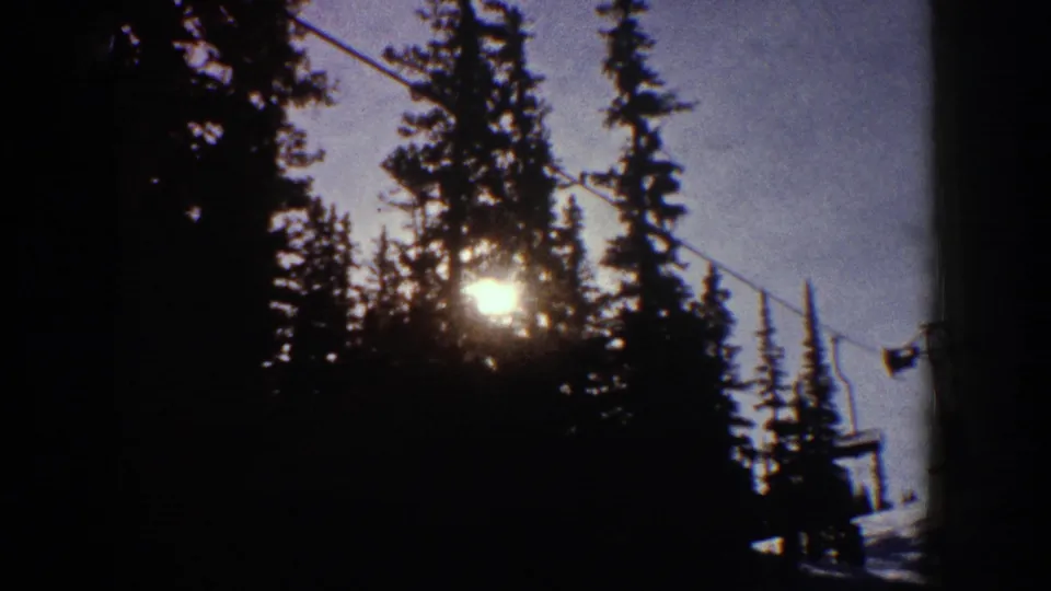 1961 Aspen winter frame with sun shining through evergreens and lift cable hardware at the edge of the ski area.