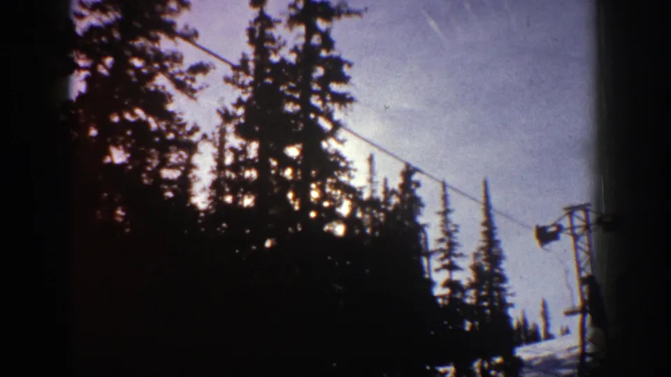 Aspen, Colorado ski-area view with dark evergreens, overhead cable, and lift hardware in grainy 8mm footage.