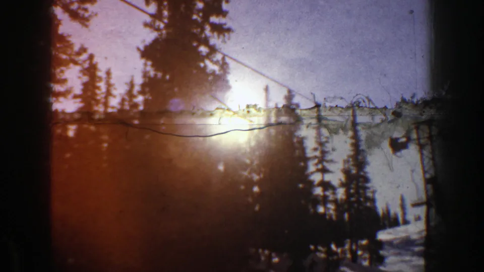 1961 Aspen ski slope detail with intense sun flare, evergreens, snow, and lift cable captured on 8mm film.