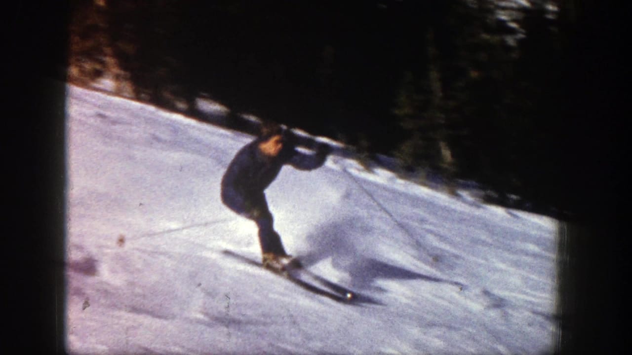 Skier crouches while moving downhill on skis across bright snow.