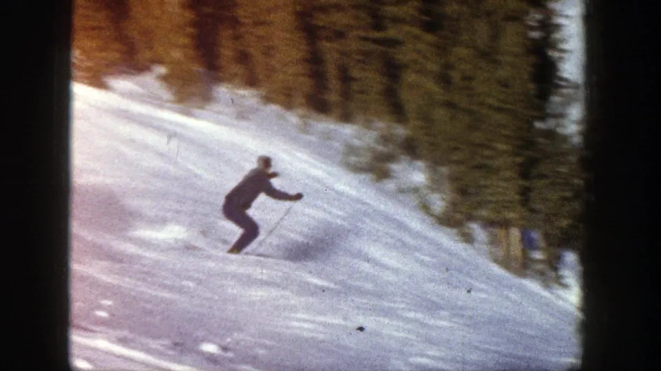 The skier continues down the Aspen slope, leaning into a maneuver against a bright snowfield and evergreen backdrop.