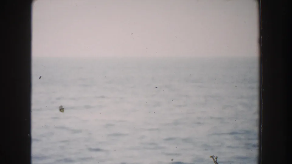 1960 Italy 8mm frame showing calm seawater meeting a distant horizon beneath a pale sky, with dust, fading, and dark film borders.