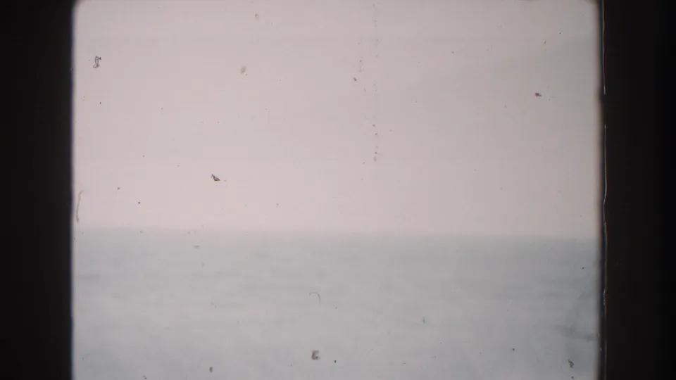1960 Italian home-movie frame showing a hazy sky and faint sea horizon, softened by 8mm grain and exposure variation.