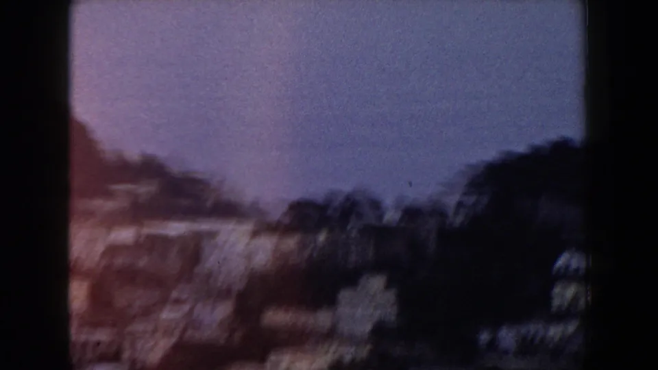Blurred 1960 Italian home-movie view of dark trees and hillside shapes beneath a bluish sky at twilight or low exposure.