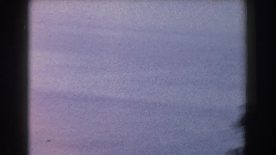 A soft, purple-blue 8mm frame from the coastal Italy footage, with faint tonal bands and a dark edge at right.
