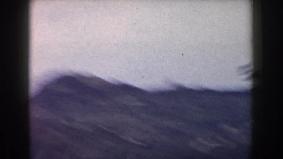 A 1960 Italy home-movie frame showing soft hills and passing terrain from a moving road perspective.
