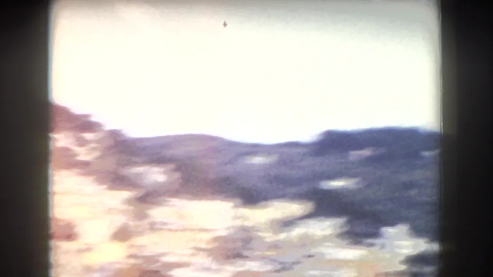 Washed 1960 Italy 8mm frame of low mountain ridges and bright sky during rapid handheld movement.