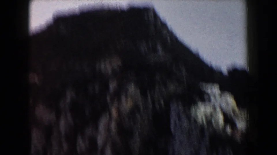 Dark, soft 1960 Italy 8mm frame showing a large rocky form or slope against a pale sky.