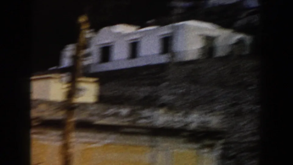 1960 Italy 8mm frame showing white-walled buildings and stonework passing quickly from a moving vehicle.