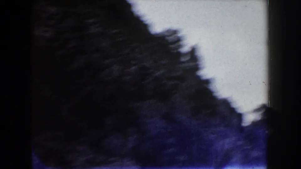 Handheld 1960 8mm Italy frame with a dark tree or rock edge silhouetted against a pale sky or bright background.